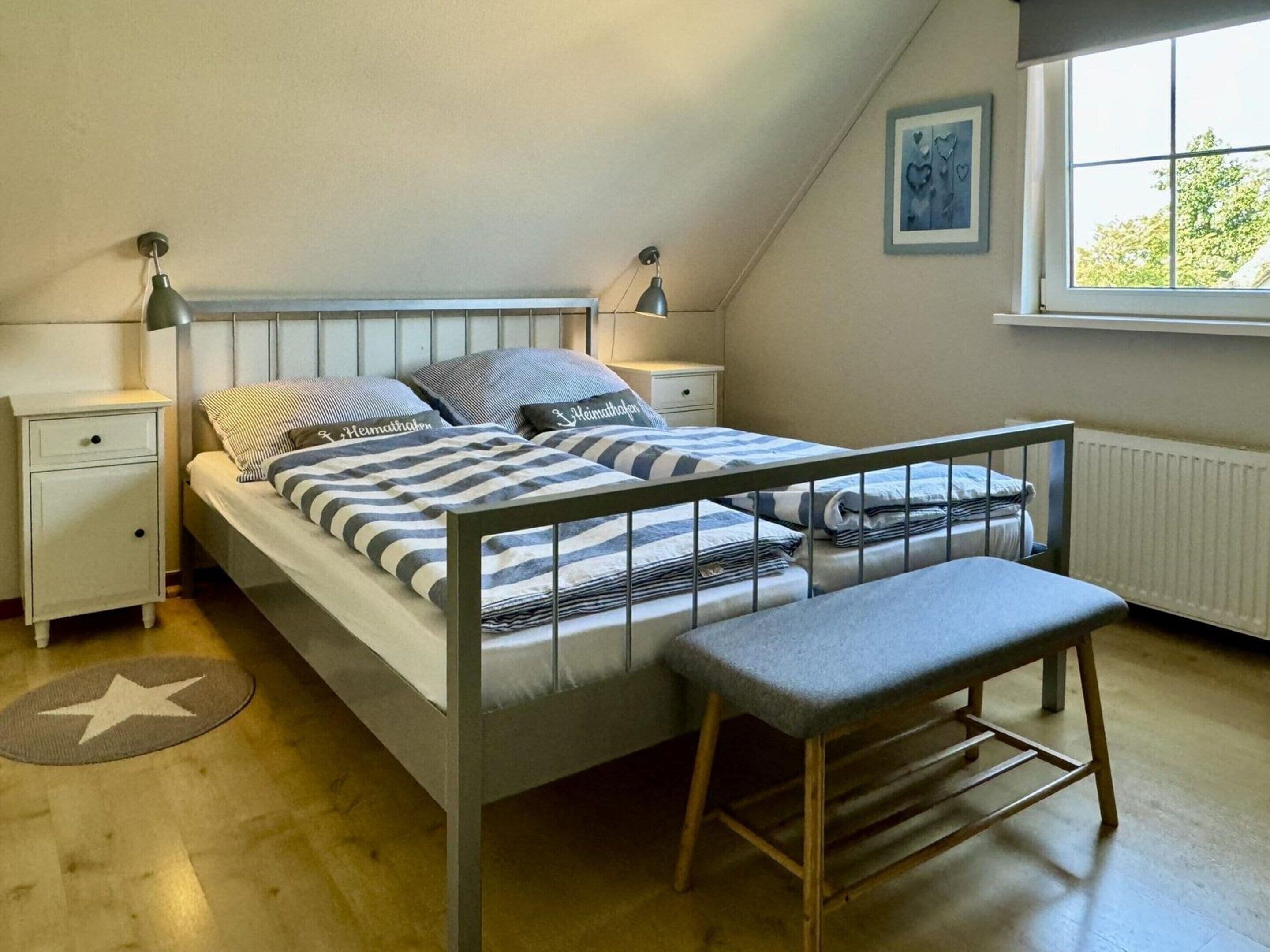 A bedroom with a bunk bed, a bedside table, a lamp, a radiator, and a window with a view of trees.