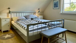 A bedroom with a bunk bed, a bedside table, a lamp, a radiator, and a window with a view of trees.