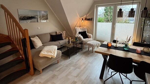 A modern loft-style living space with a loft bed, a dining area with a wooden table, and a cozy seating area with a sofa and armchairs. - Fewo Schill und Mee(h)r, modern apartment in the center, pets allowed. (Wangerland)