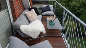A balcony with a sofa, cushions, a small table, and a vase. - Fewo Schill und Mee(h)r, modern apartment in the center, pets allowed. (Wangerland)