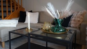 A modern living room with a glass coffee table, a white candle, decorative vases, and a staircase in the background. - Fewo Schill und Mee(h)r, modern apartment in the center, pets allowed. (Wangerland)
