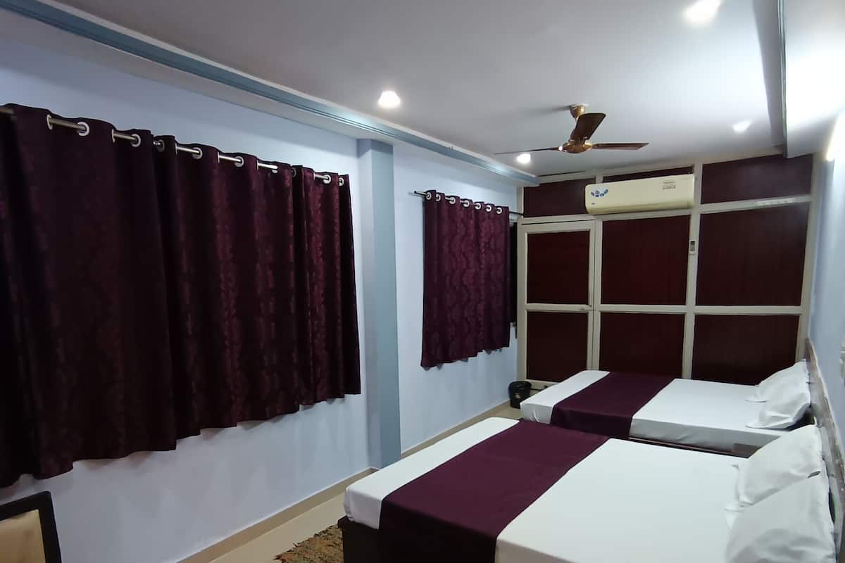 Habitación de hotel con dos camas, ventilador de techo, unidad de aire acondicionado y ventana con cortinas.