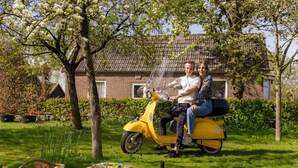 A couple on a yellow scooter in a garden with a picnic setup.