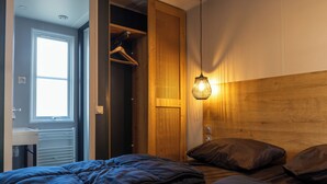 A bedroom with a bed, a wooden headboard, a hanging light fixture, and a closet with a hanging rack.