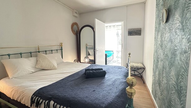 Une chambre à coucher avec un lit, une table de chevet, un miroir et une vue sur l’extérieur.