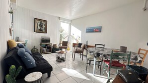 Un salon avec un canapé, une table à manger, des chaises, un cactus, une horloge et une radio.