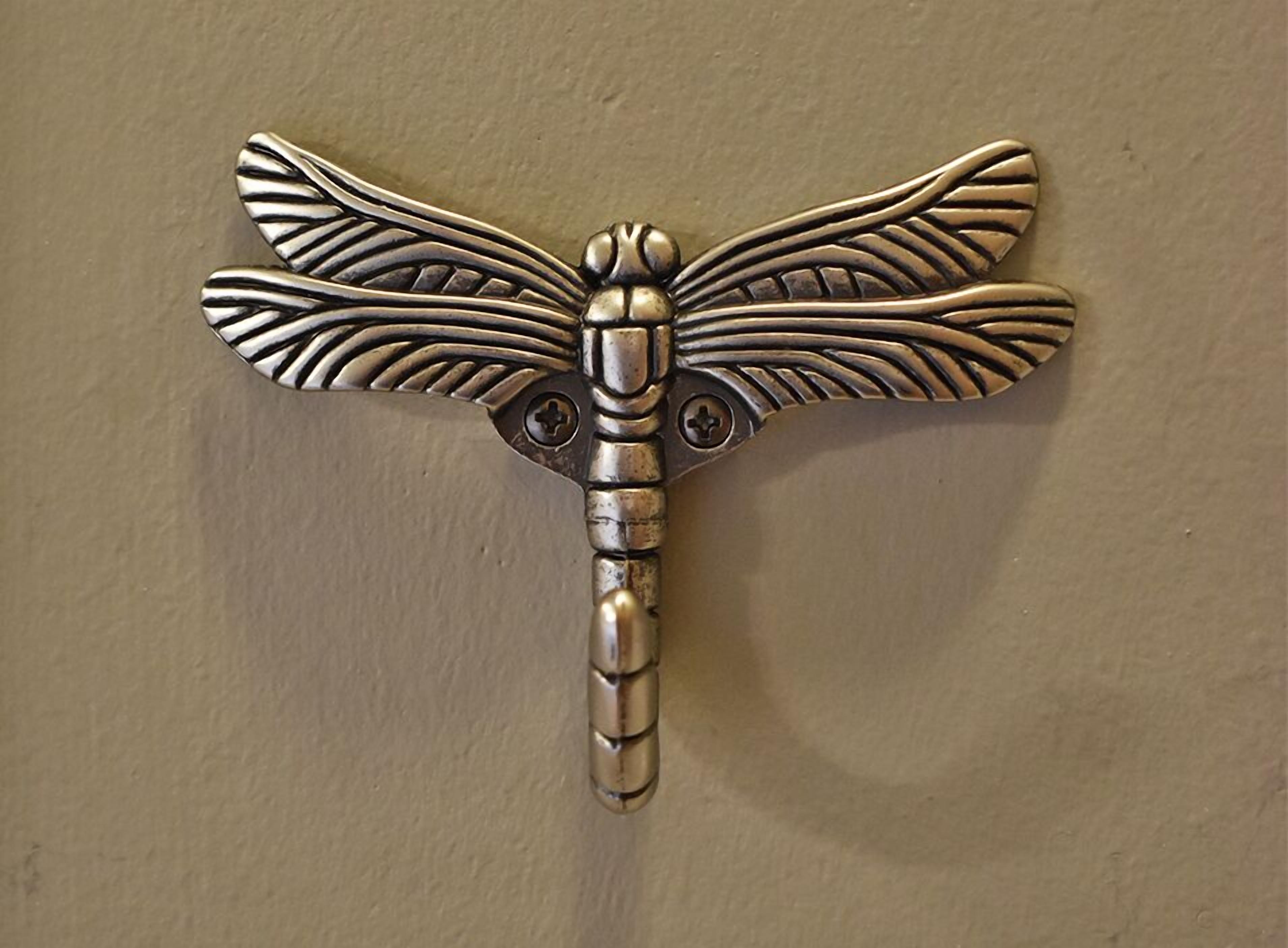 A metallic dragonfly-shaped object with intricate wing patterns and a segmented body, mounted on a wall.
