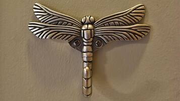 A metallic dragonfly-shaped object with intricate wing patterns and a segmented body, mounted on a wall.