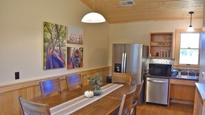 A dining area with a wooden table, chairs, and a vase with flowers. There is a refrigerator and a microwave in the kitchen area. - Johnson's Shut-ins State Park (Middle Brook)