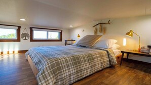 Quarto com cama grande, duas mesas de cabeceira, um criado-mudo, uma janela e uma luminária fixada na parede.