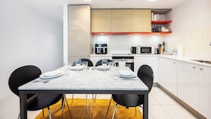 A modern kitchen with white cabinets, a marble countertop, and a dining area with a table set for four. - Hoola Cove Executive One Bed Apartment (London)