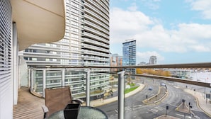 A modern building with a curved facade, a balcony with a glass table and chairs, and a view of a city intersection. - Hoola Cove Executive One Bed Apartment (London)