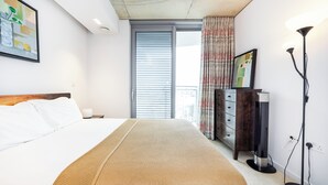 A hotel room with a bed, a nightstand, a dresser, a standing heater, and a window with blinds. - Hoola Cove Executive One Bed Apartment (London)