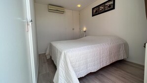 A bedroom with a bed, a wardrobe, an air conditioning unit, and a wall-mounted picture.