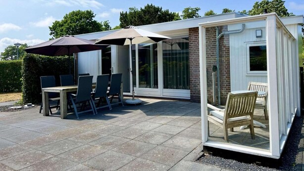 A covered patio area with a table and chairs, a glass enclosure, and a brick wall.