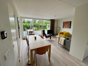 Una sala de estar moderna con comedor, televisor y un sillón amarillo.