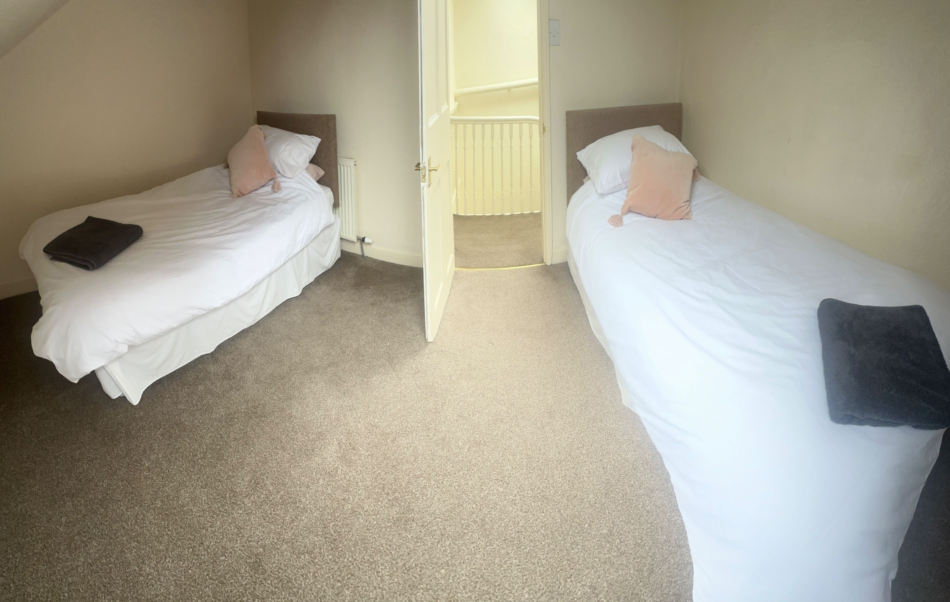 A room with two single beds, each with a pillow and a folded blanket.