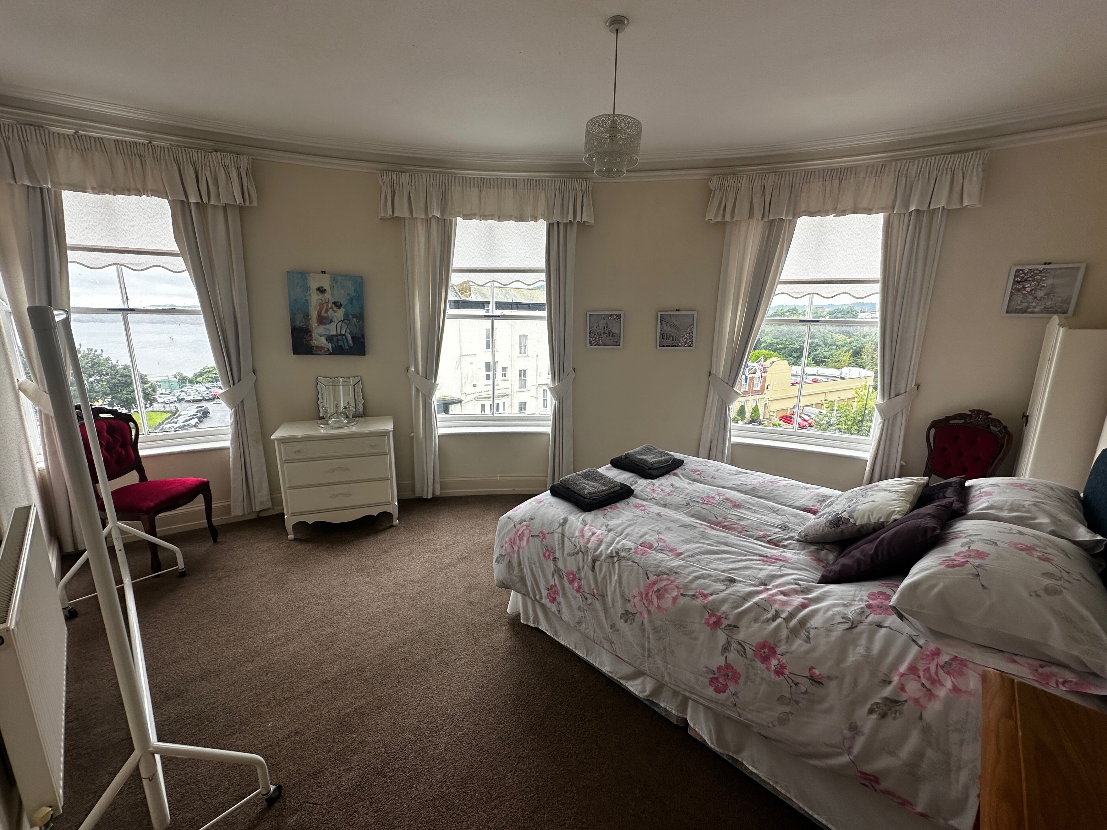 Een slaapkamer met een bed, een dressoir, een stoel en uitzicht op zee.