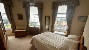 Une chambre à coucher avec un grand lit, une commode, une commode à tiroirs et une fenêtre avec des rideaux.
