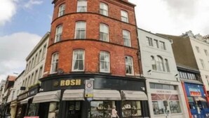 Un immeuble d’angle dont le rez-de-chaussée abrite un magasin appelé « Rosh ».
