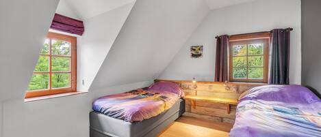 Un dormitorio con techo inclinado, una cama, un banco y dos ventanas con cortinas.