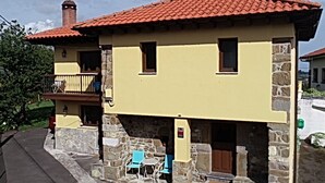 Ein zweistöckiges Haus mit rotem Ziegeldach, Steinunterbau und einem Balkon mit blauen Stühlen.