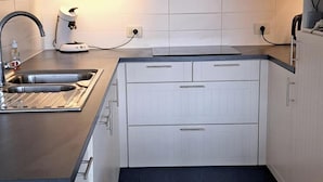 Moderni keittiö, jossa on vaaleat puukalusteet, musta työtaso ja ruostumattomasta teräksestä valmistettu pesuallas.