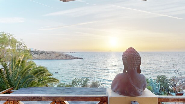 Eine Buddha-Statue mit Blick auf die Küste bei Sonnenuntergang.