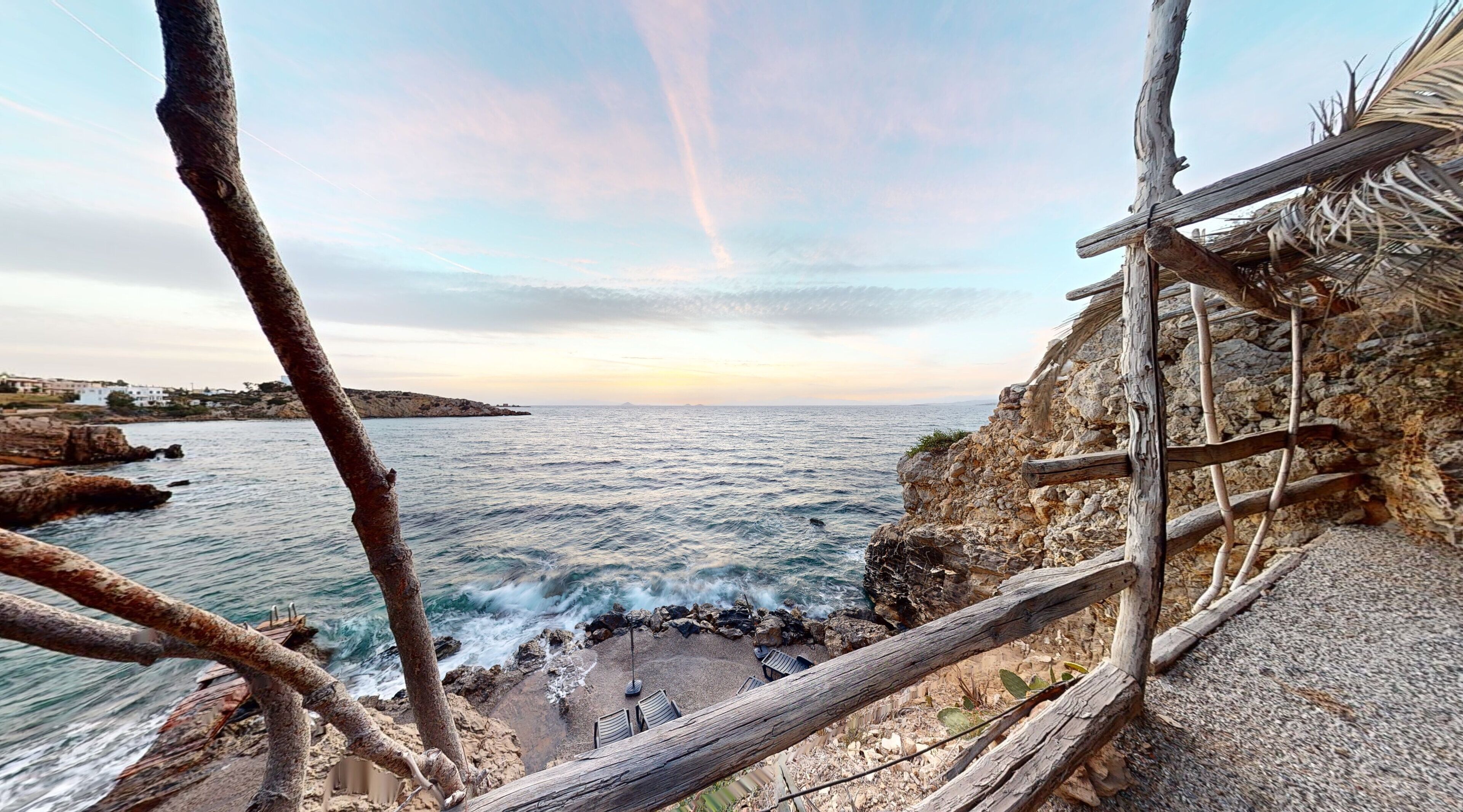 A coastal view with a rocky shoreline, a wooden fence, and a small seating area with chairs.