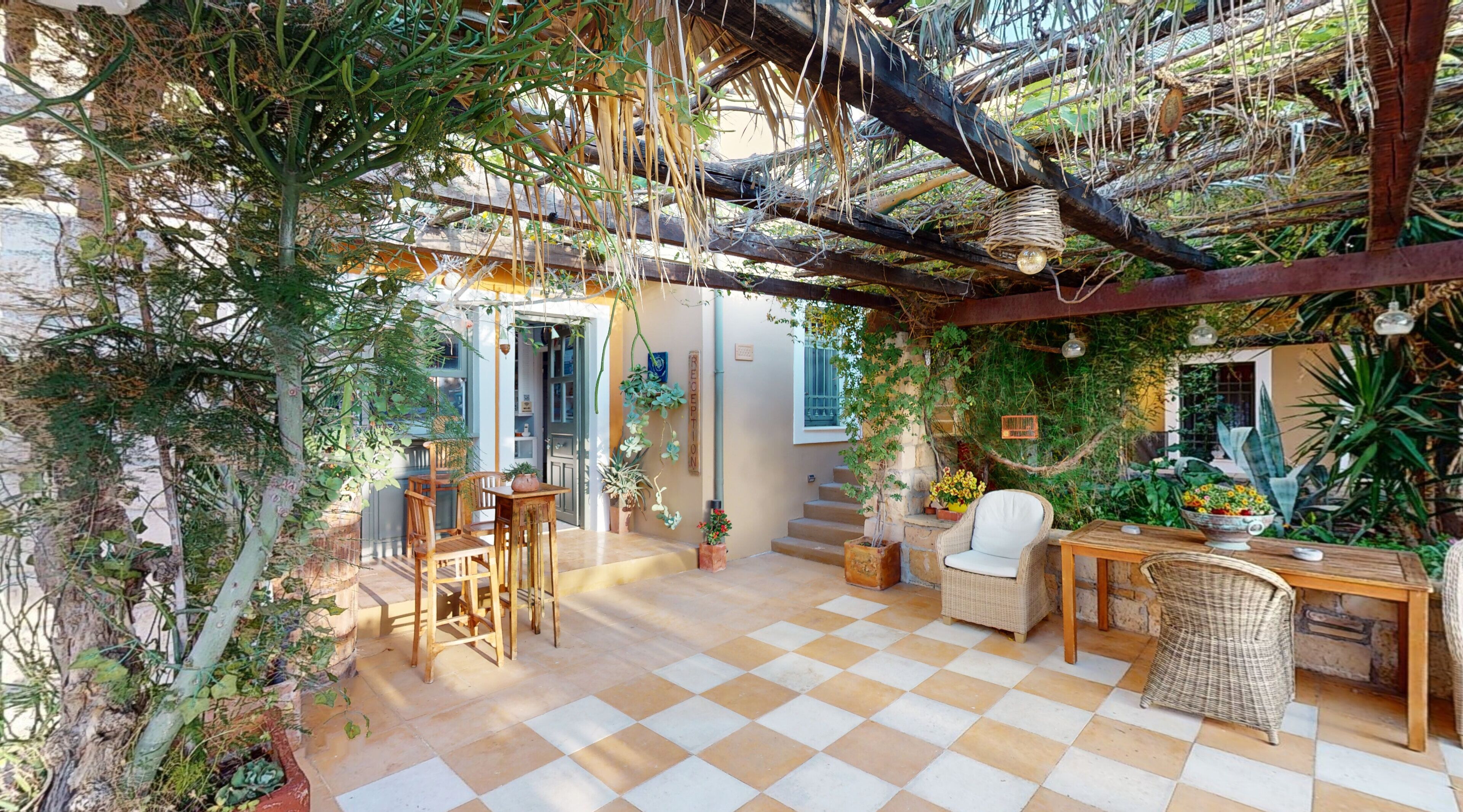 A cozy patio area with a checkered floor, wooden furniture, and lush greenery.