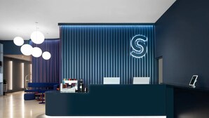 Egy modern recepciós pult függőleges világítópanellel és egy neonfényben világító „S” betűvel.