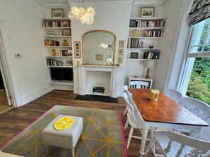A room with a fireplace, bookshelves, a dining table, and a window with a view.