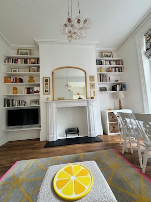 A living room with a fireplace, bookshelves, a television, and a decorative orange slice on the rug.