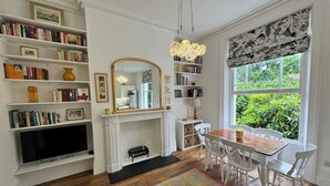 A room with a fireplace, bookshelves, a dining table, and a large window with a view of greenery.