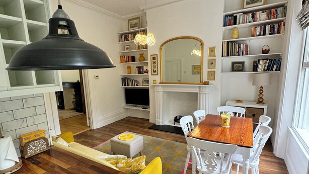A modern kitchen with a wooden island, white chairs, a dining table, and a bookshelf filled with books.