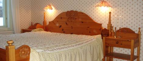 Un dormitorio con una cama de madera, dos lámparas de noche, una mesita de noche y un papel tapiz con motivos florales.