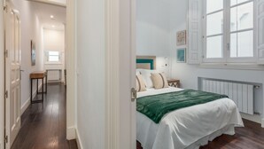 A bedroom with a bed, a window, a radiator, and a door leading to another room.