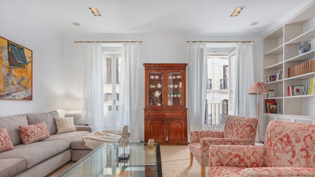 A living room with a sofa, armchairs, a glass coffee table, a wooden cabinet, and a bookshelf.