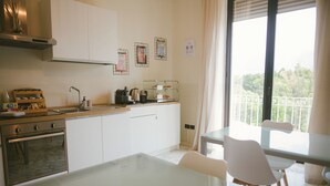 Una cocina moderna con armarios blancos, horno de acero inoxidable, cafetera y mesa de vidrio.