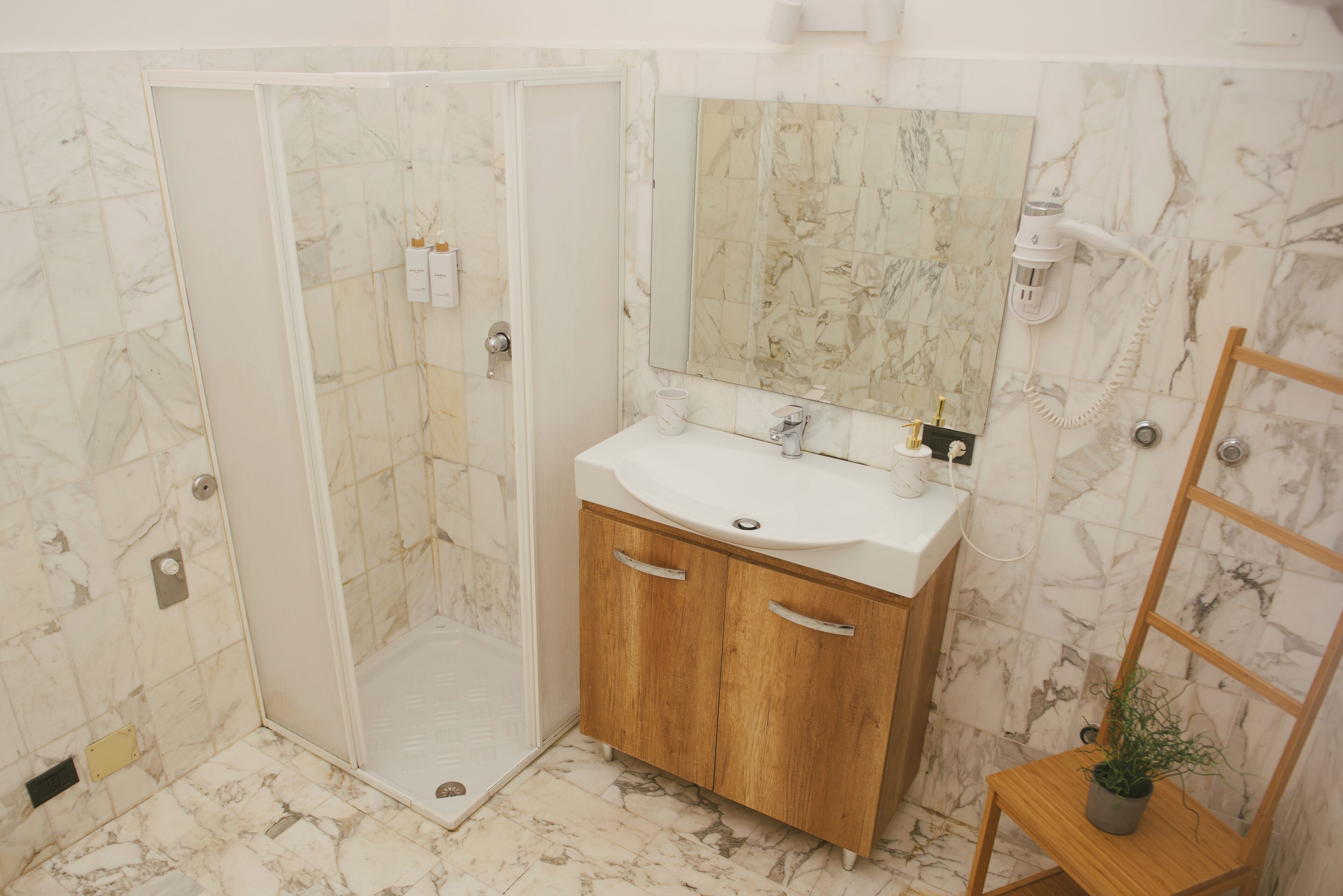 Ein Badezimmer mit Dusche, Waschbecken, Holzschränken, einem Spiegel und einem Blumentopf.