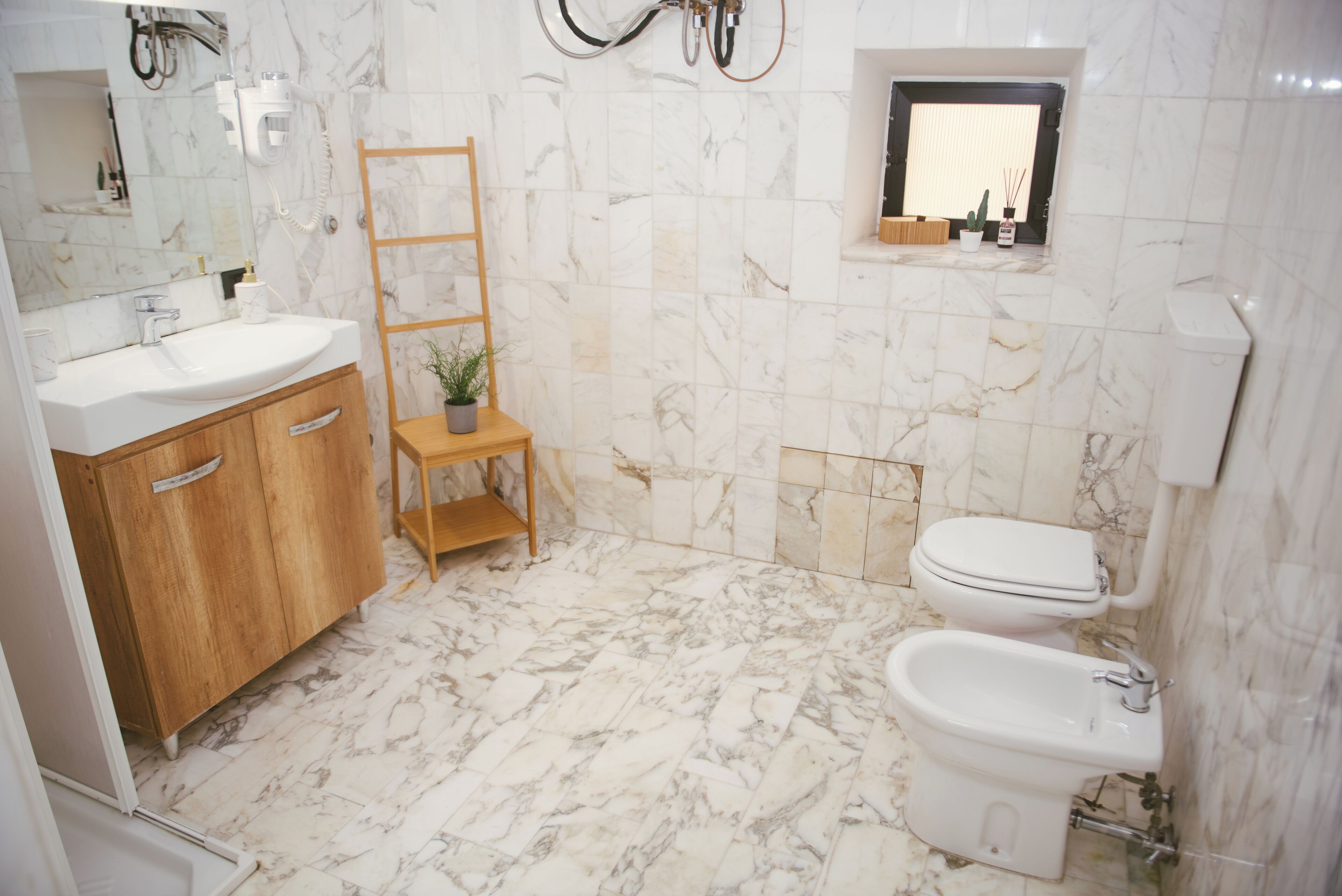 Une salle de bain avec un sol en marbre, des meubles en bois, un lavabo, des toilettes et un bidet.