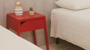 A bedroom with a red nightstand, a white bed, and a small potted plant.