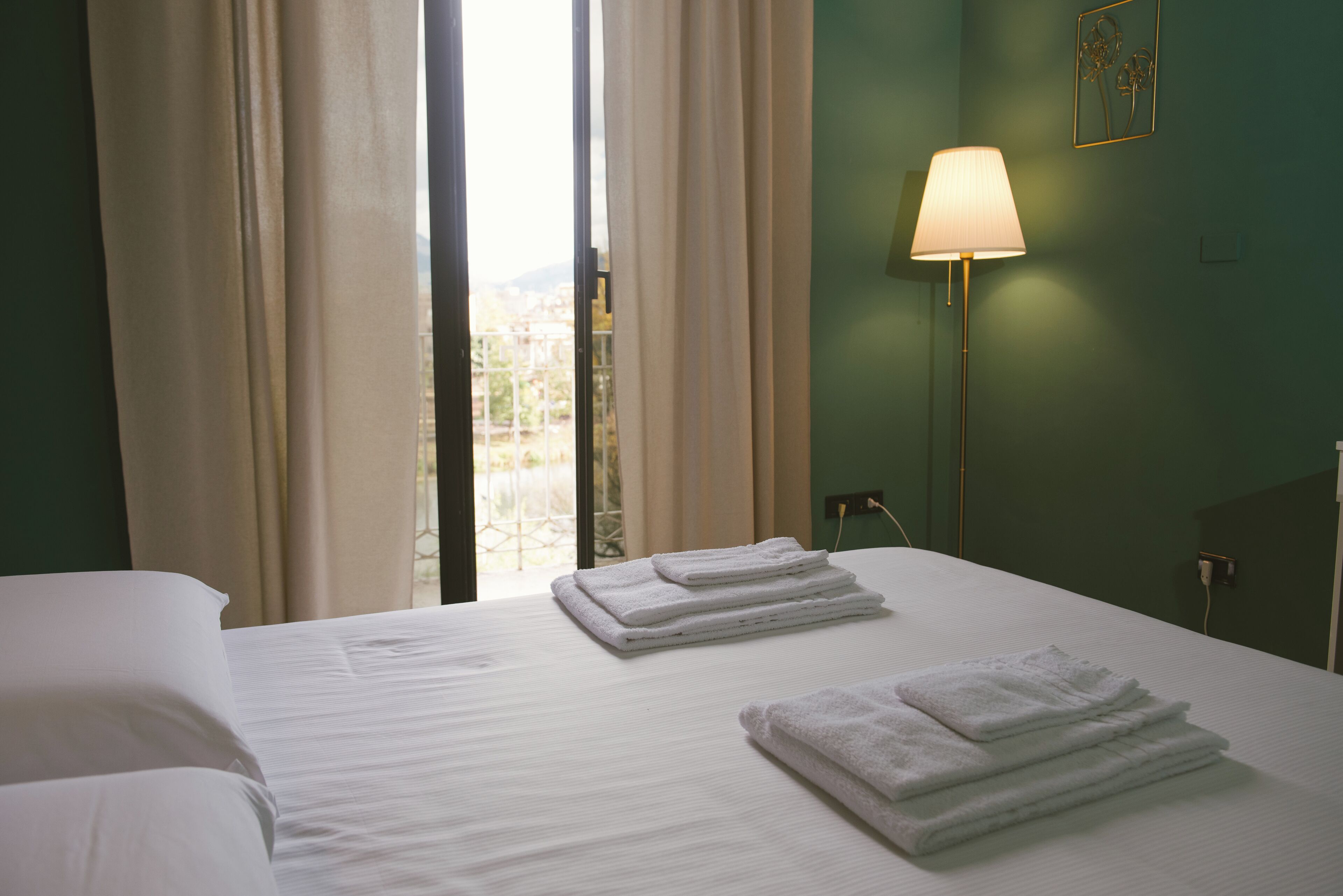 A hotel room with a bed, two towels, a lamp, and a view through the window.