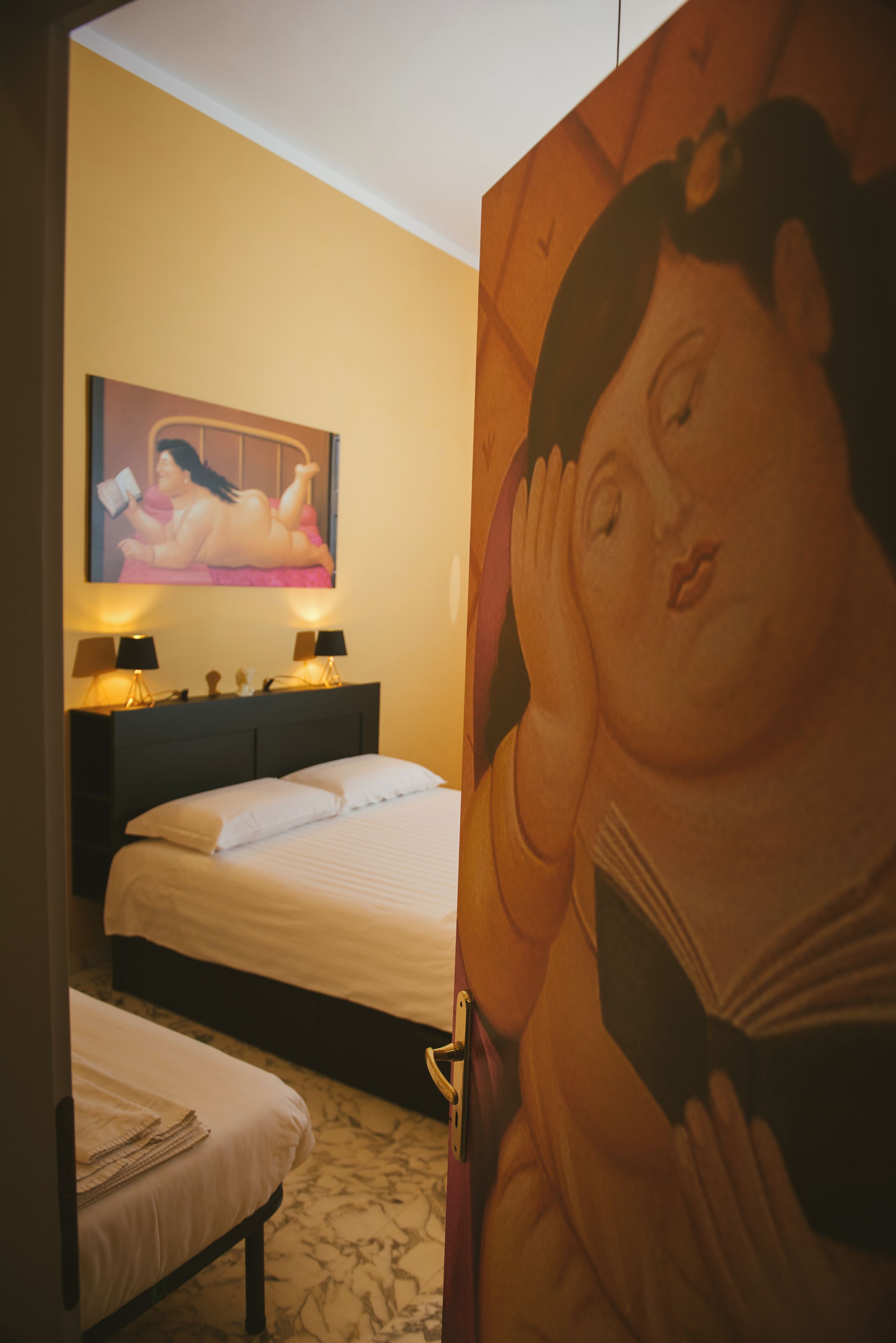 Ein Hotelzimmer mit Bett, Nachttischlampen, einem kleinen Tisch und einem großen Gemälde an der Wand.