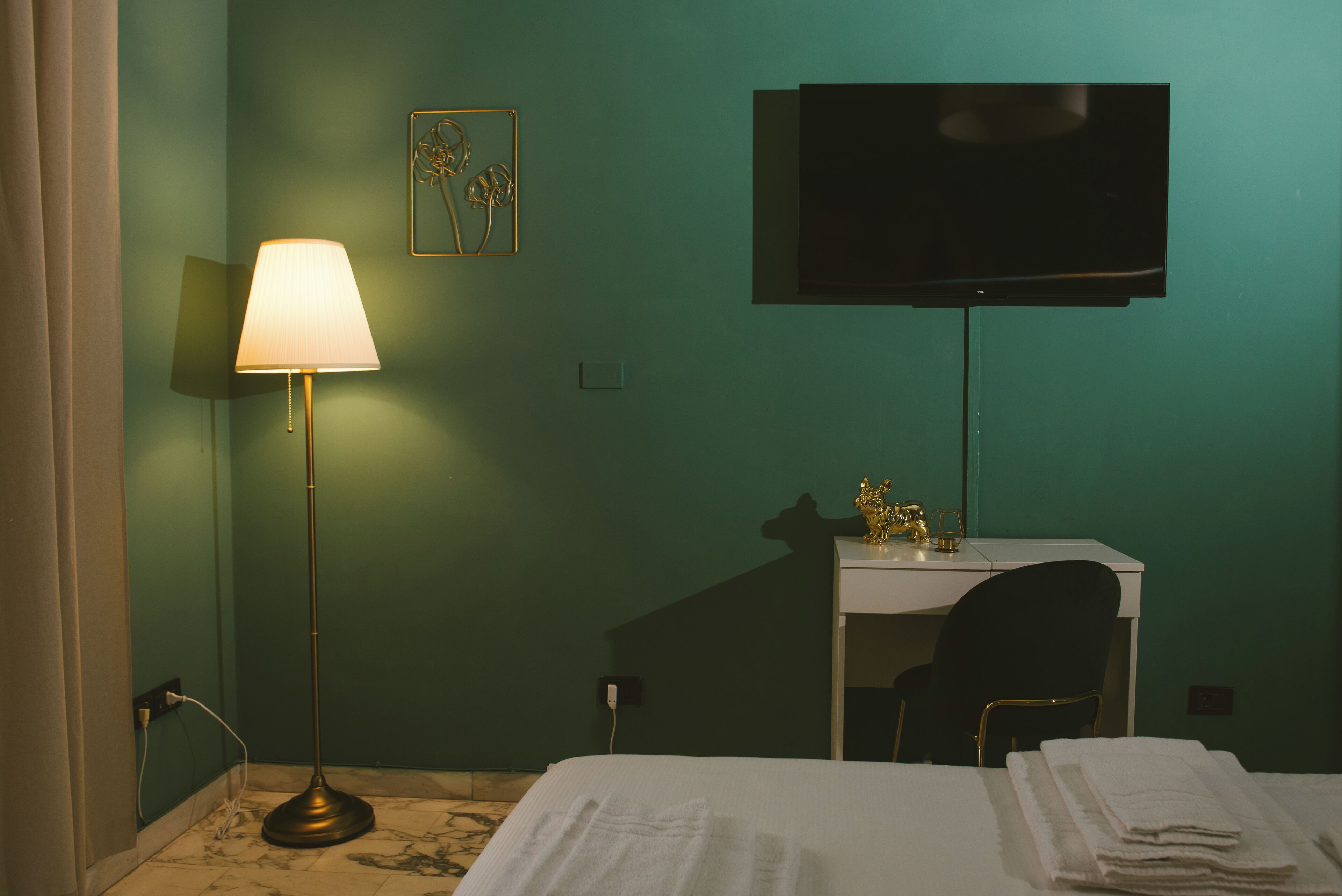 A hotel room with a bed, a desk with a chair, a television, and a floor lamp.