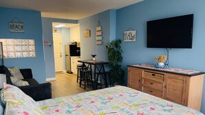 Une chambre avec un lit, un bureau, une télévision et un coin cuisine.
