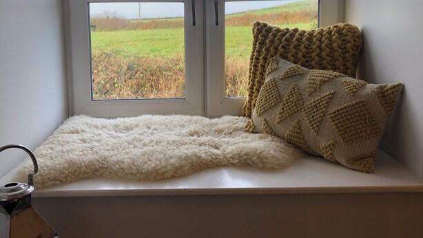A window seat with a white furry rug, a knitted pillow, and a metal lantern. - Renovated farmhouse, 5 mins from the sea (Ferwig)