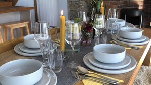 A dining table set with white plates, glasses, and cutlery, a lit candle, and a rustic brick wall in the background. - Renovated farmhouse, 5 mins from the sea (Ferwig)
