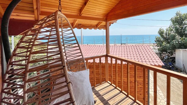 Un balcón de madera con una hamaca colgante, techo de tejas y vista al mar.