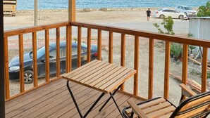 Una terraza de madera con una mesa y sillas, con vista a una playa donde se ven coches y una persona caminando.